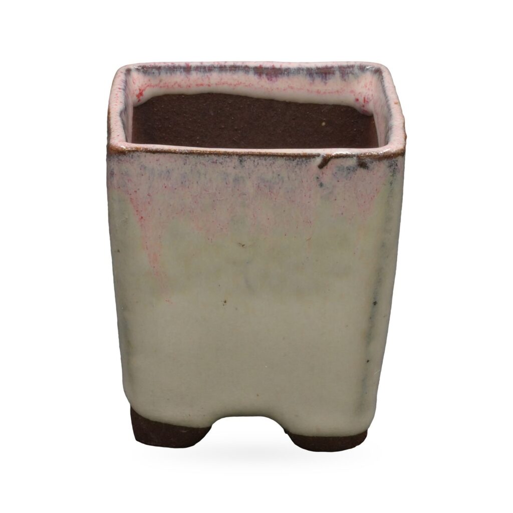 Cream glazed square footed pot with pink-purple blush at the rim and dark brown clay feet