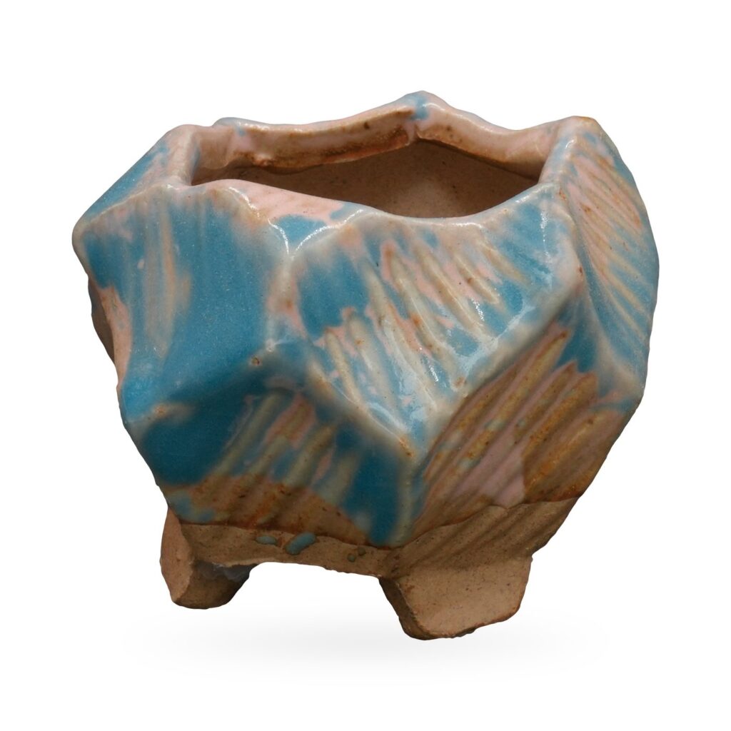 Small faceted turquoise and blush-pink glazed pot with a zigzag rim on small clay feet