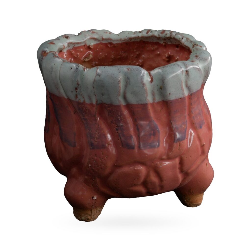 Glossy coral-red rounded footed pot with thick pale blue-white glaze around a wavy rim