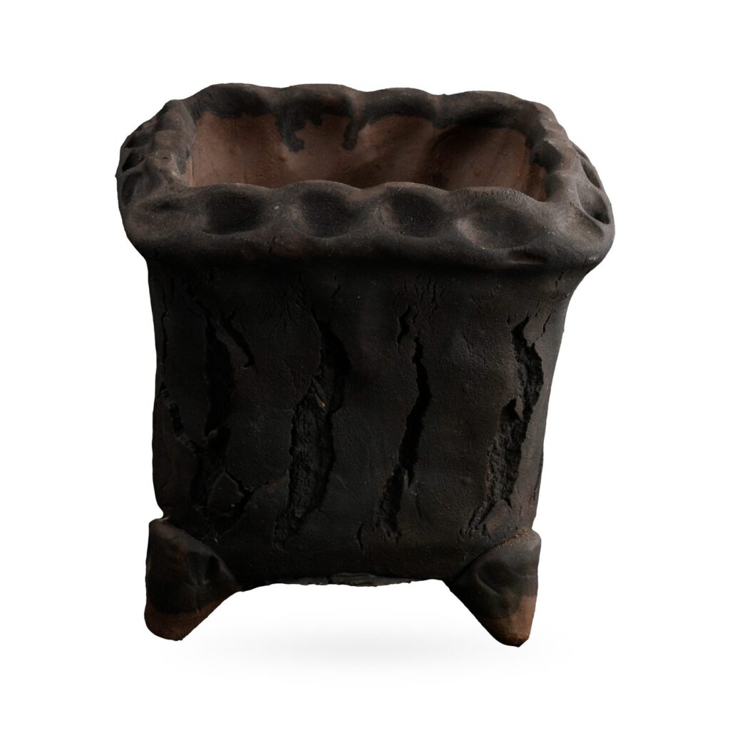 Rough matte charcoal-black square footed pot with cracked bark texture and dimpled rim