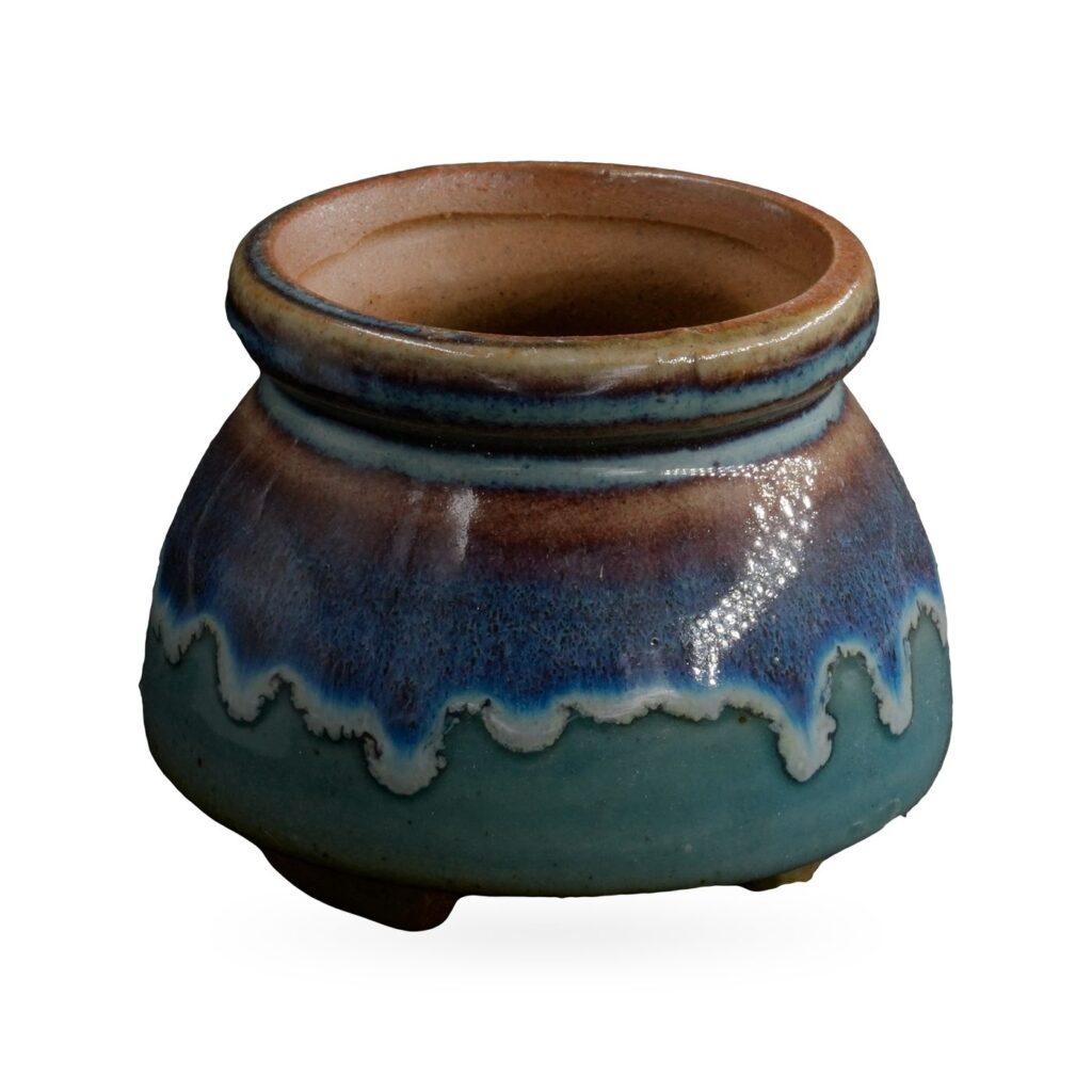 Squat round footed pot with glossy teal base, blue-purple drip band and speckled brown rolled rim