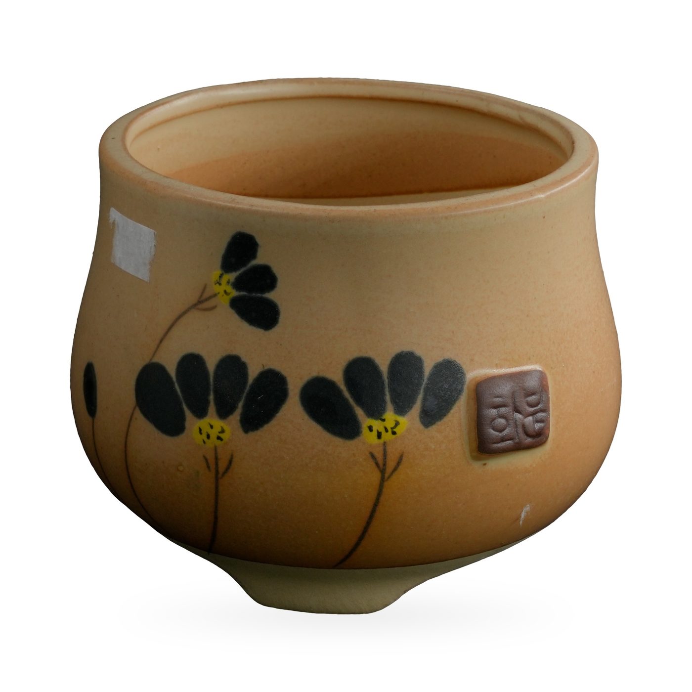Ochre-yellow footed pot with painted black flowers and a small brown seal-style plaque
