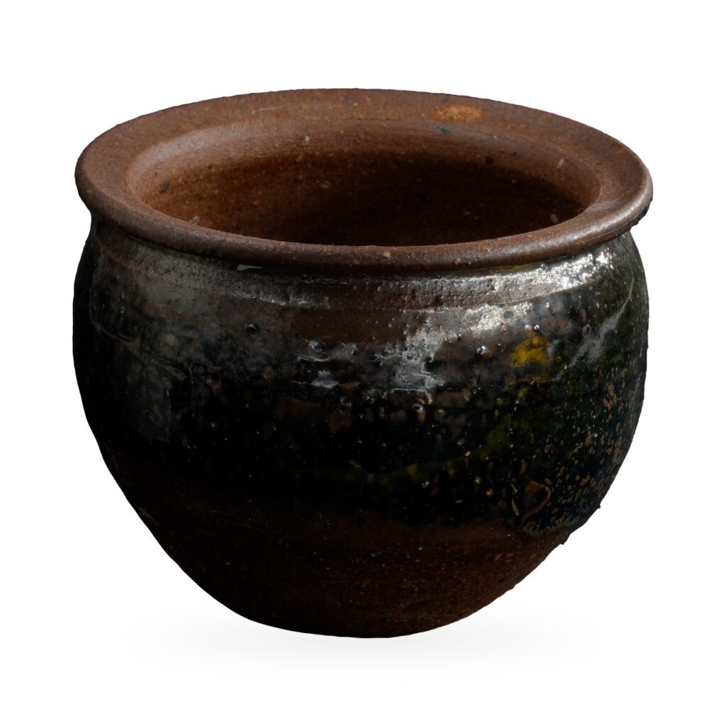 Round pot in glossy black glaze with rust-brown speckles, a wide flared brown rim and bare clay base