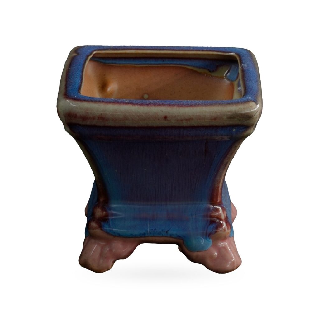 Square pot in glossy blue glaze streaked with purple, with a beige-edged rim, on glossy pink cloud-shaped feet