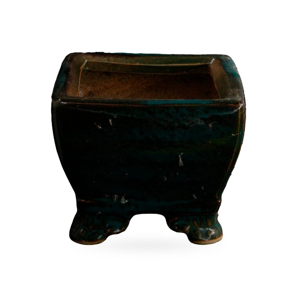 Square pot in glossy dark teal-green glaze over black, with a stepped rim and small decorative feet
