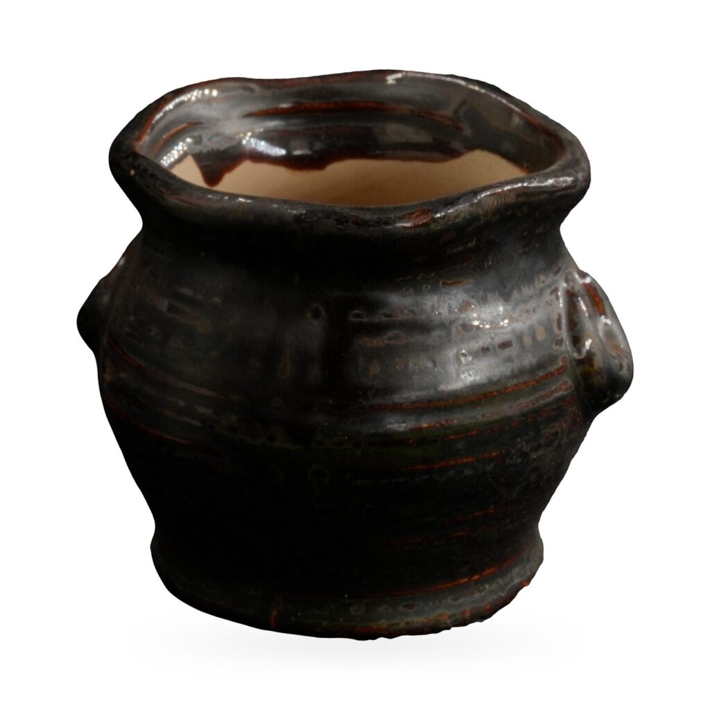 Small black-brown glazed rustic pot with textured body, wavy rim and two small loop ears