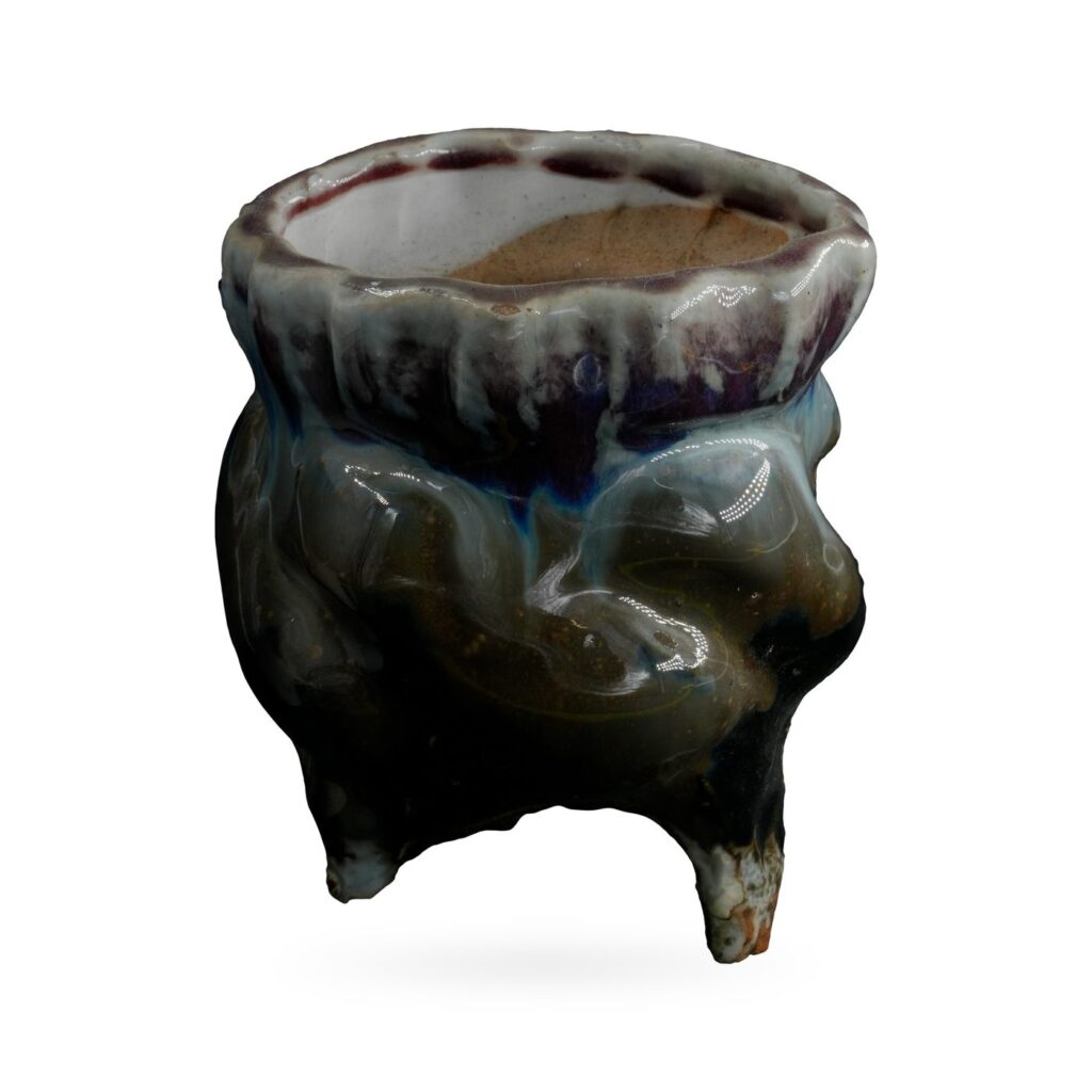 Footed pot with glossy black body and blue-white drip glaze from a scalloped plum rim
