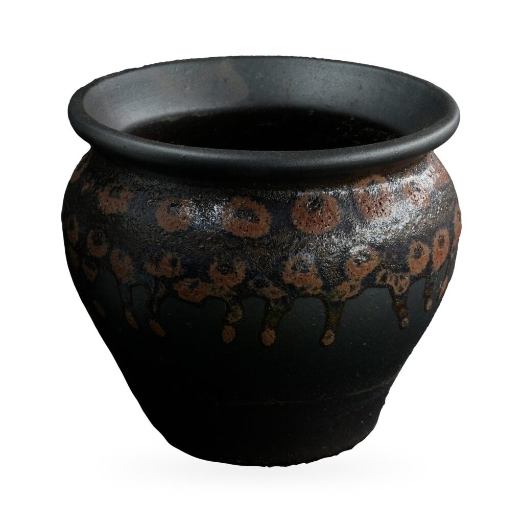 Round matte black pot with a rust-orange spotted drip glaze band and rolled rim