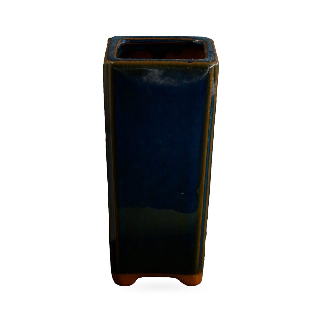 Tall slim square pot in glossy navy-blue glaze with amber-brown edges and small corner feet