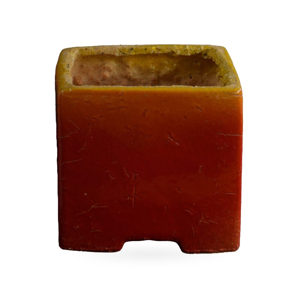 Glossy square pot fading from orange to red with a mustard-yellow rim and small corner feet