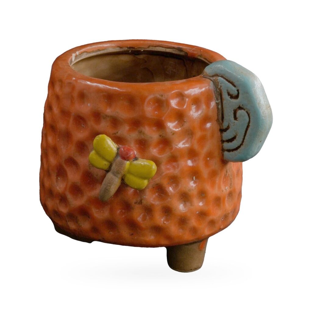 Orange dimpled footed pot with a light-blue cloud-swirl tab and yellow-winged dragonfly