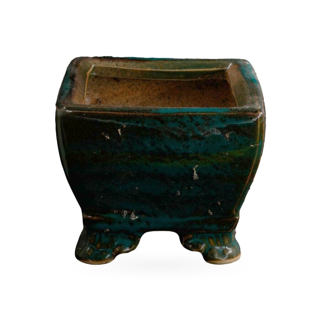 Square pot in glossy dark teal-green glaze over black, with a stepped rim and small decorative feet