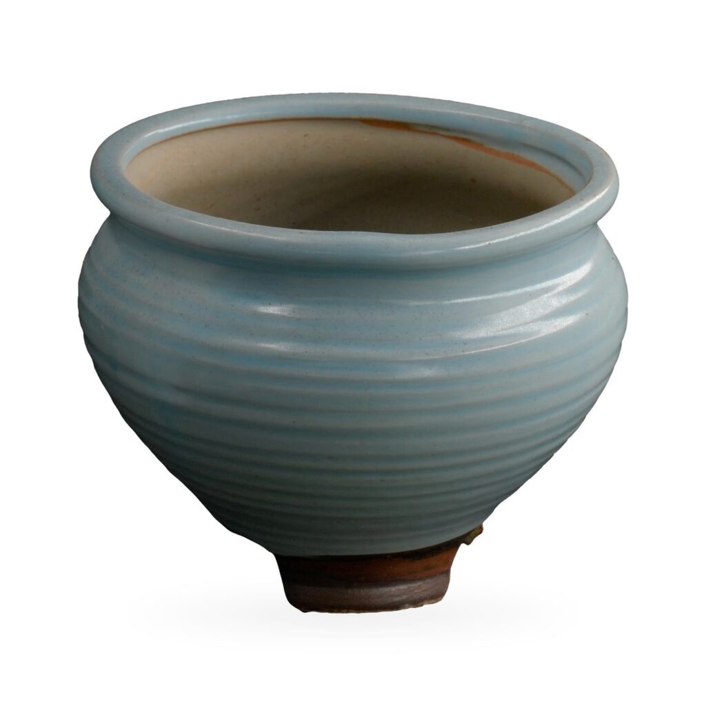 Pale blue ribbed glazed pot with rolled rim on small dark brown feet