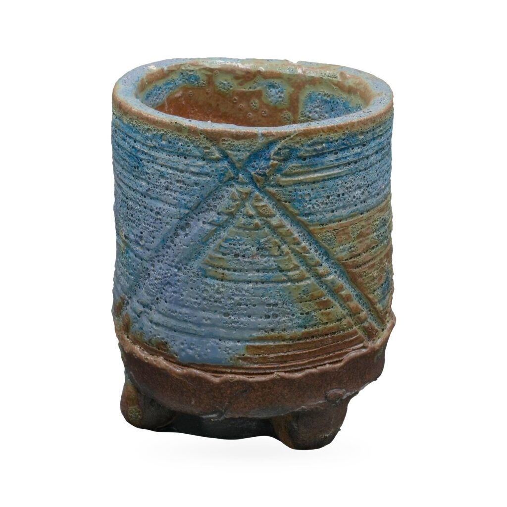 Tall blue-green cylinder pot with pitted lava-style glaze, raised X pattern and dark brown footed base