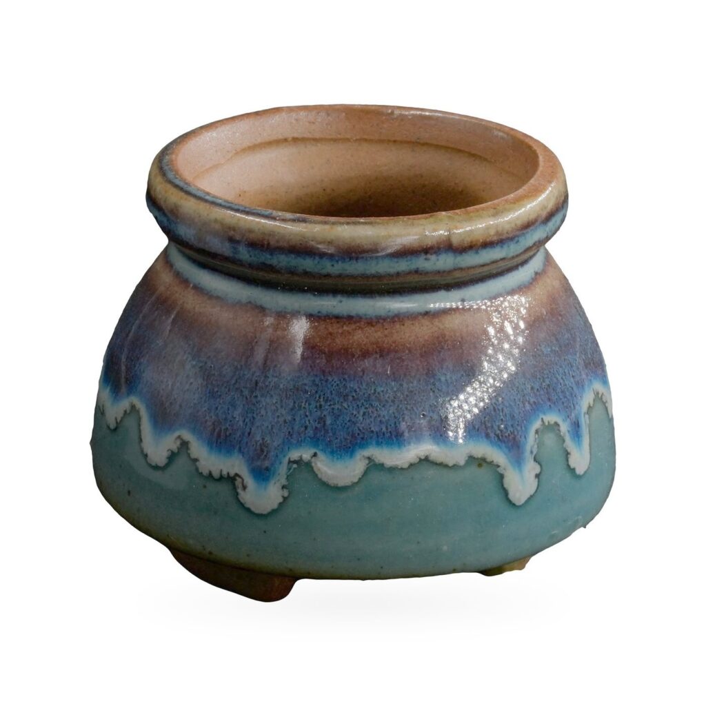 Squat round footed pot with glossy teal base, blue-purple drip band and speckled brown rolled rim