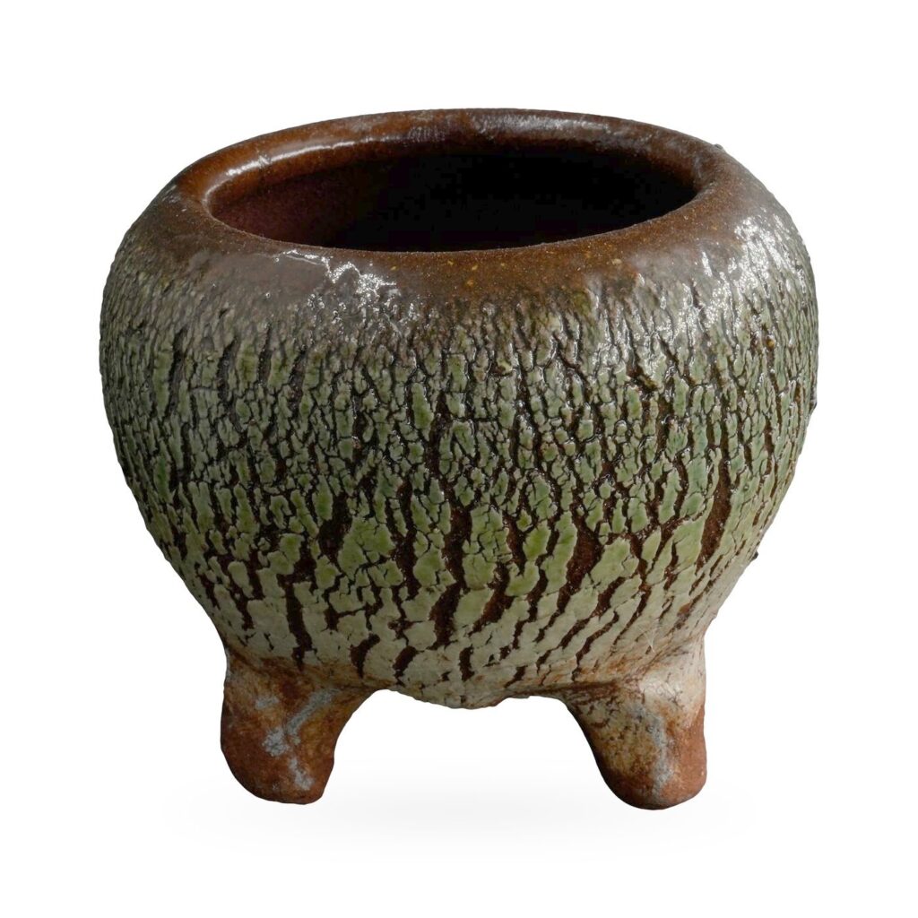 Round pot with a bark-like moss green crackle texture over dark brown, on short terracotta-toned feet
