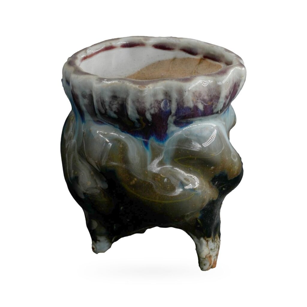 Footed pot with glossy black body and blue-white drip glaze from a scalloped plum rim