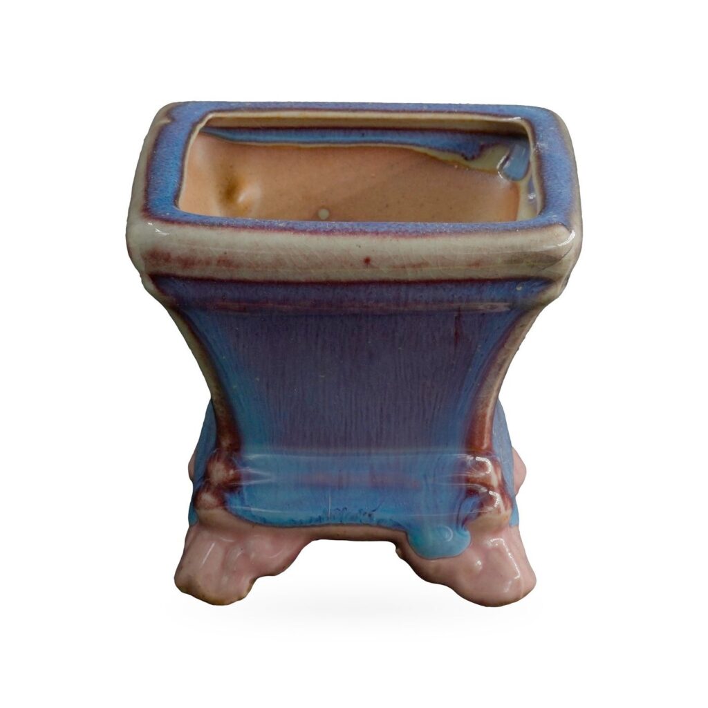Square pot in glossy blue glaze streaked with purple, with a beige-edged rim, on glossy pink cloud-shaped feet
