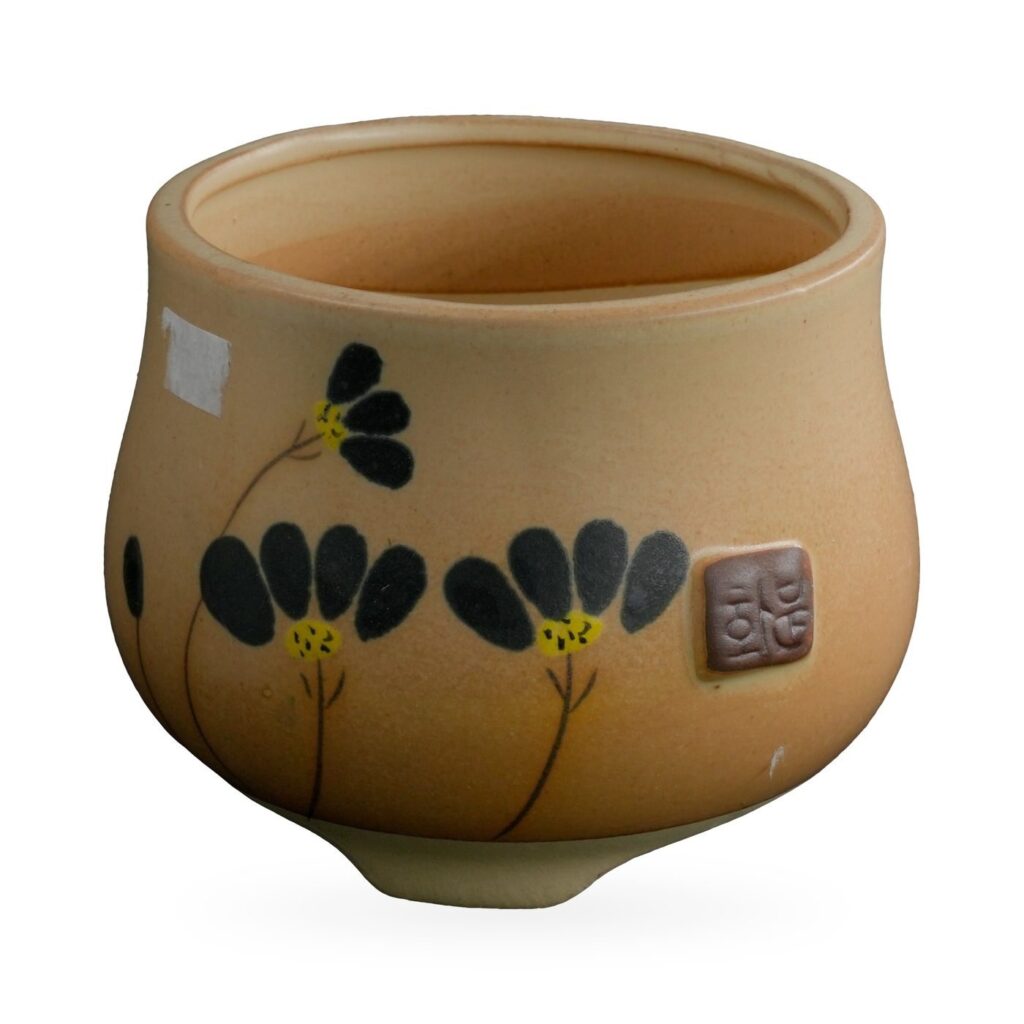 Ochre-yellow footed pot with painted black flowers and a small brown seal-style plaque