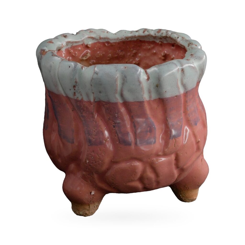 Glossy coral-red rounded footed pot with thick pale blue-white glaze around a wavy rim