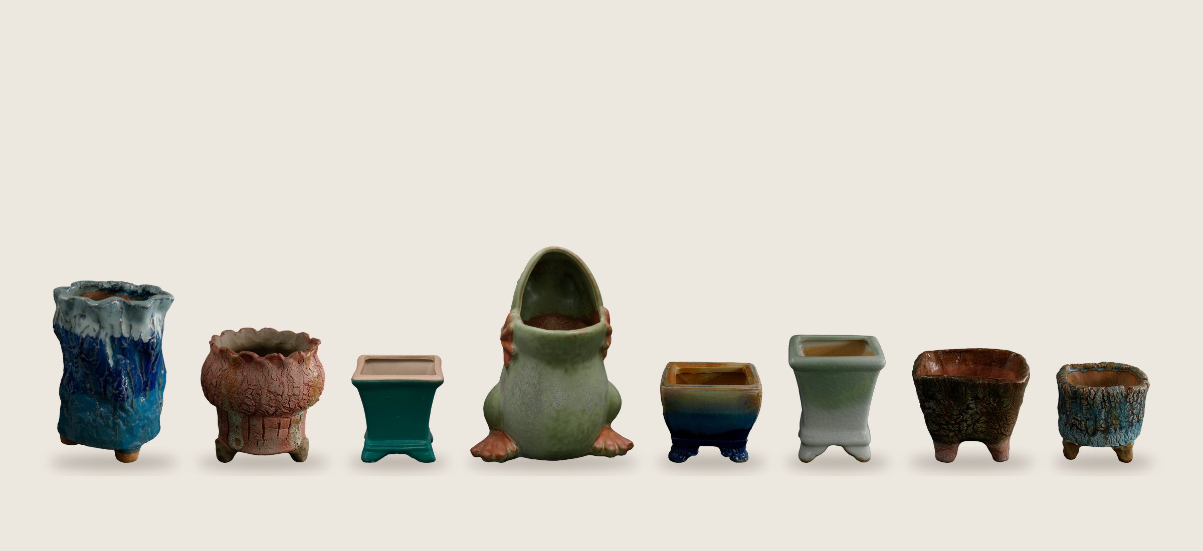 A row of small glazed ceramic succulent pots and a frog planter